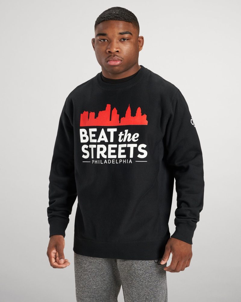 A young man wearing a black sweatshirt with BEAT the STREETS PHILADELPHIA printed in white and red paired with gray sweatpants