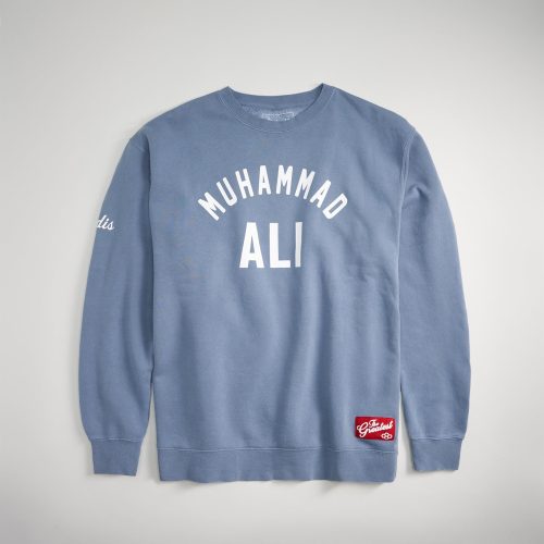 A light blue sweatshirt featuring the name Muhammad Ali prominently displayed in bold white letters across the front with a red tag at the bottom reading The Greatest