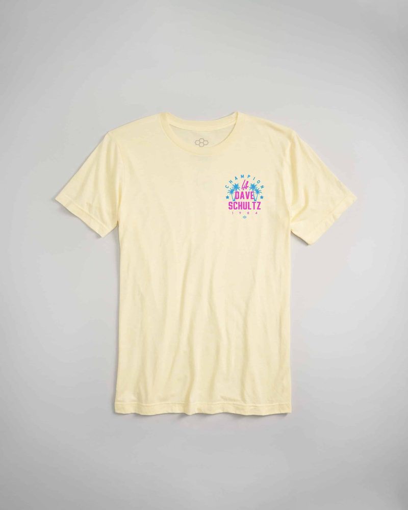 A light yellow t-shirt featuring colorful graphic text and palm tree designs celebrating Dave Schultz an iconic figure from 1984