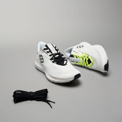 A pair of modern running shoes in white with contrasting black and neon yellow laces set against a neutral background featuring textured mesh uppers and a sleek design