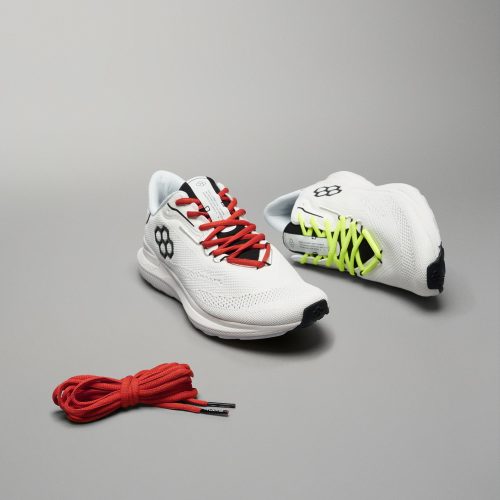 A pair of modern athletic shoes in white featuring red and neon green laces accompanied by a separate bundle of red shoelaces