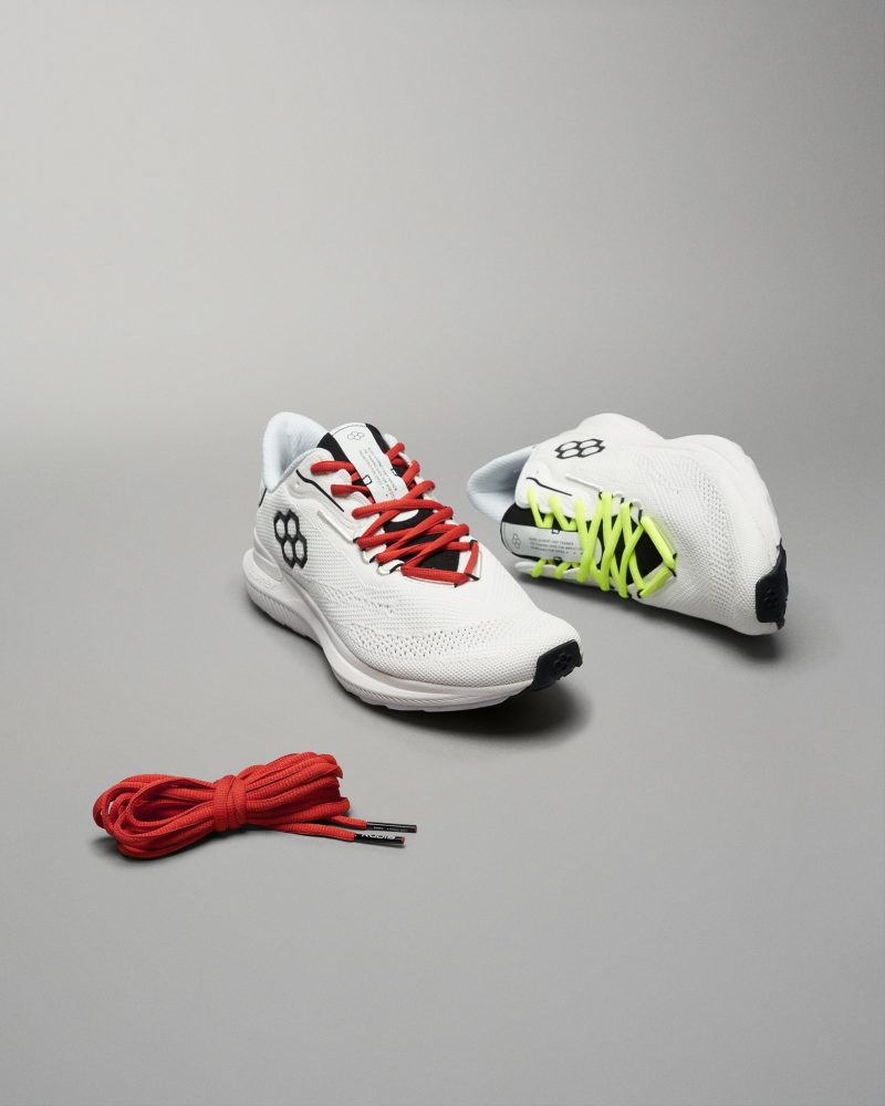 A pair of modern athletic shoes in white featuring red and neon green laces accompanied by a separate bundle of red shoelaces