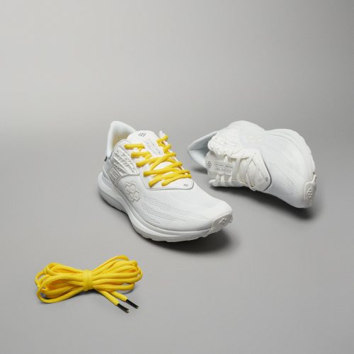 A pair of stylish white athletic shoes with yellow laces accompanied by an extra set of yellow laces on a neutral background